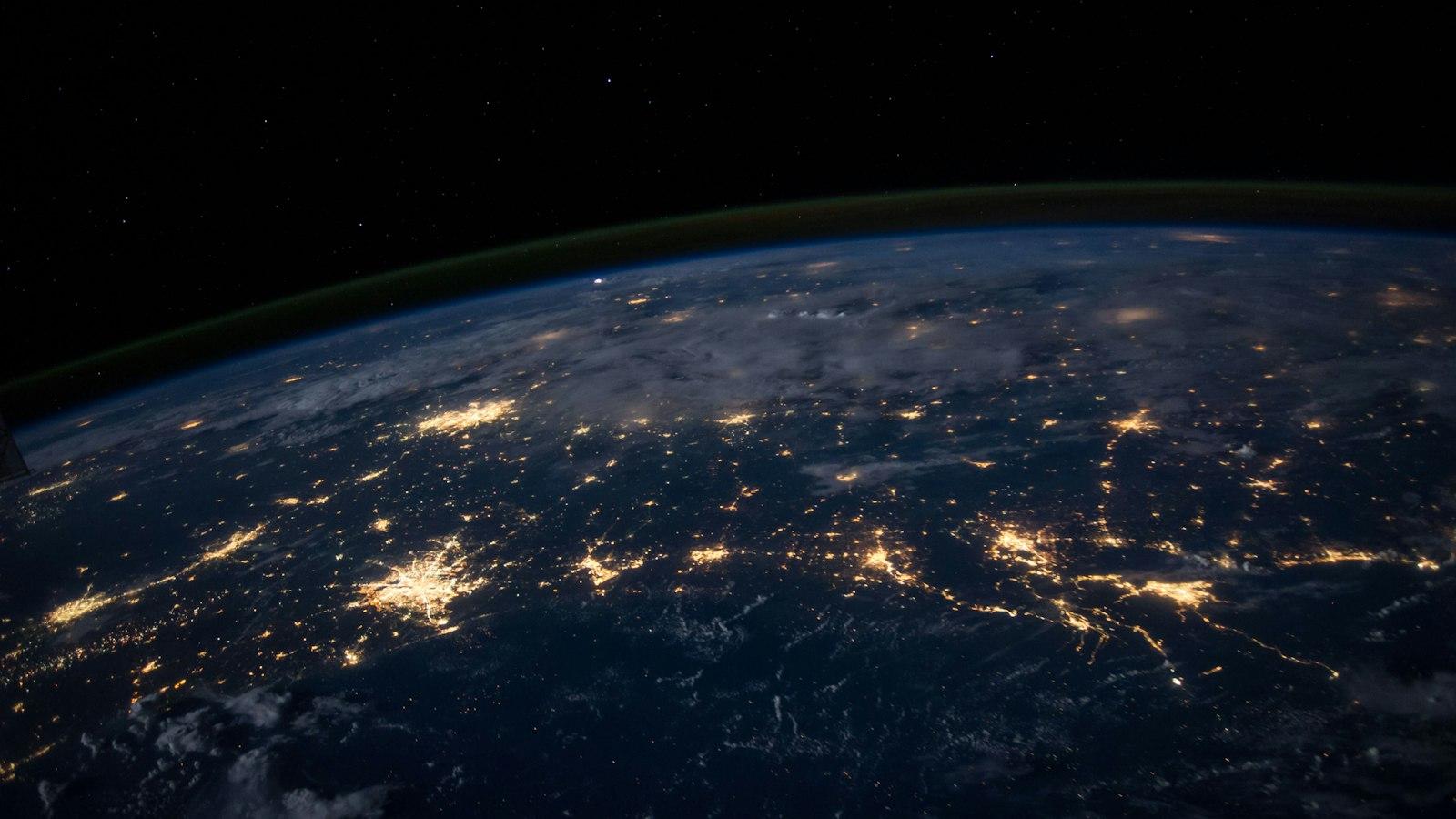 The Earth at night seen from space, with city lights forming glowing networks